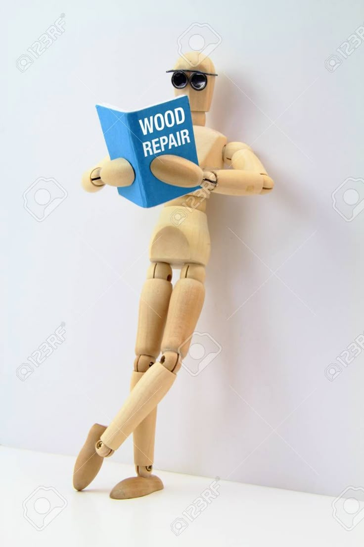 a wooden mannequin holding a book that says wood repair on it stock photo