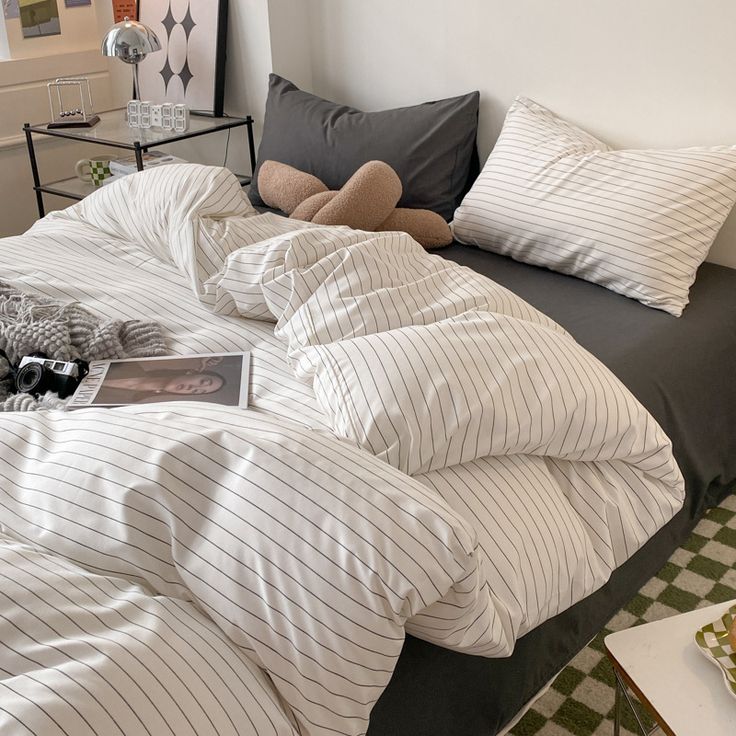 an unmade bed with white and grey striped comforter, pillows and blankets on it