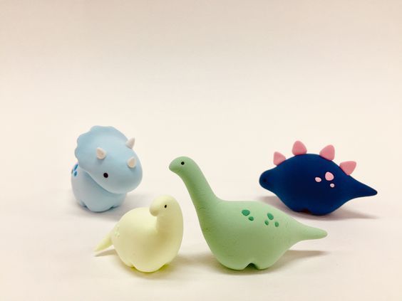 three toy dinosaurs sitting next to each other on a white surface with one dinosaur in the foreground