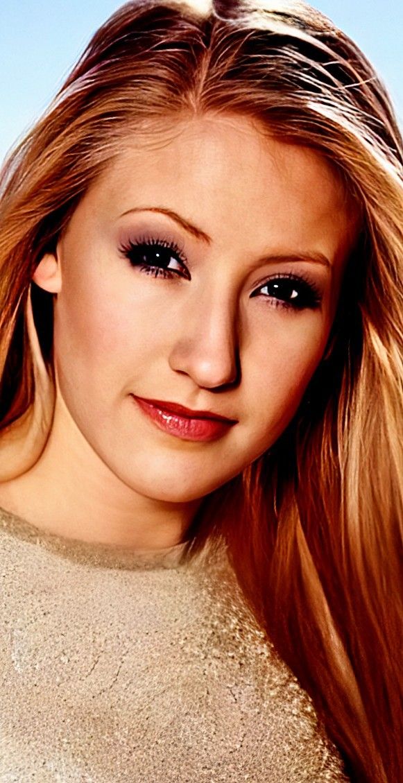 a woman with long blonde hair and black eyeshadow posing for a photo in front of a blue sky