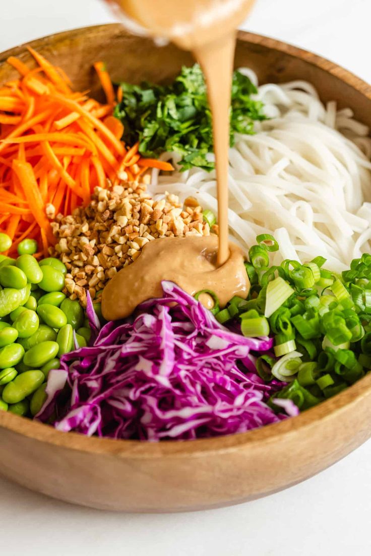 a wooden bowl filled with vegetables and sauce being poured into the salad dressing in it