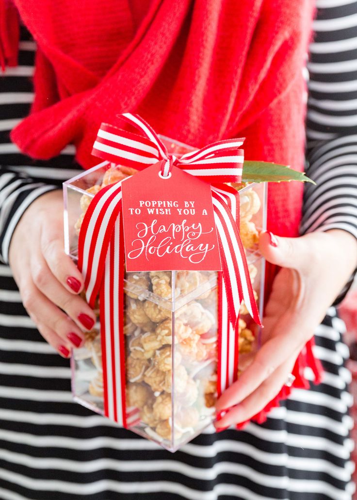 a woman holding a box filled with popcorn and a red card that says poppin'n wish you a merry holiday