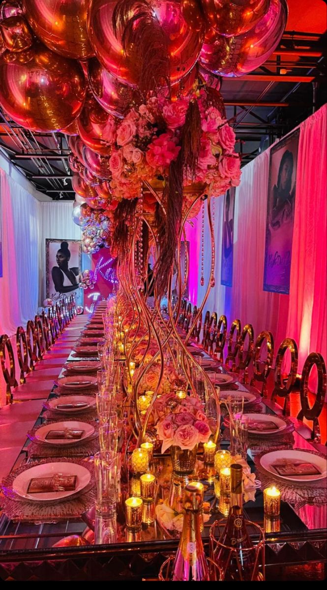 a long table is set with pink and gold balloons in the center, along with plates and silverware