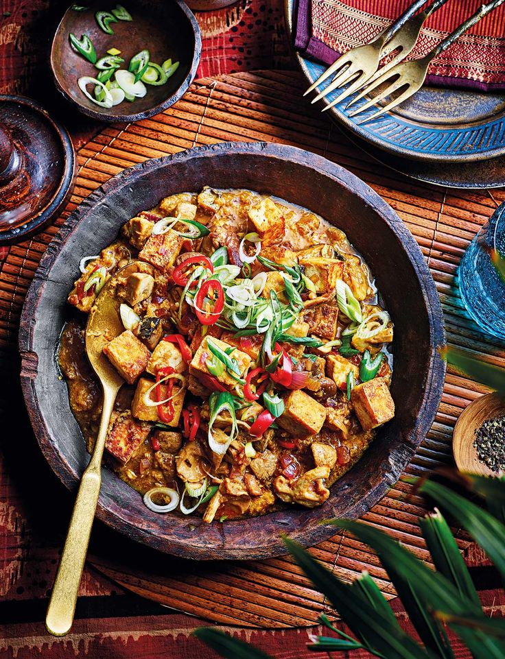 a bowl filled with tofu and vegetables on top of a wooden table next to other plates