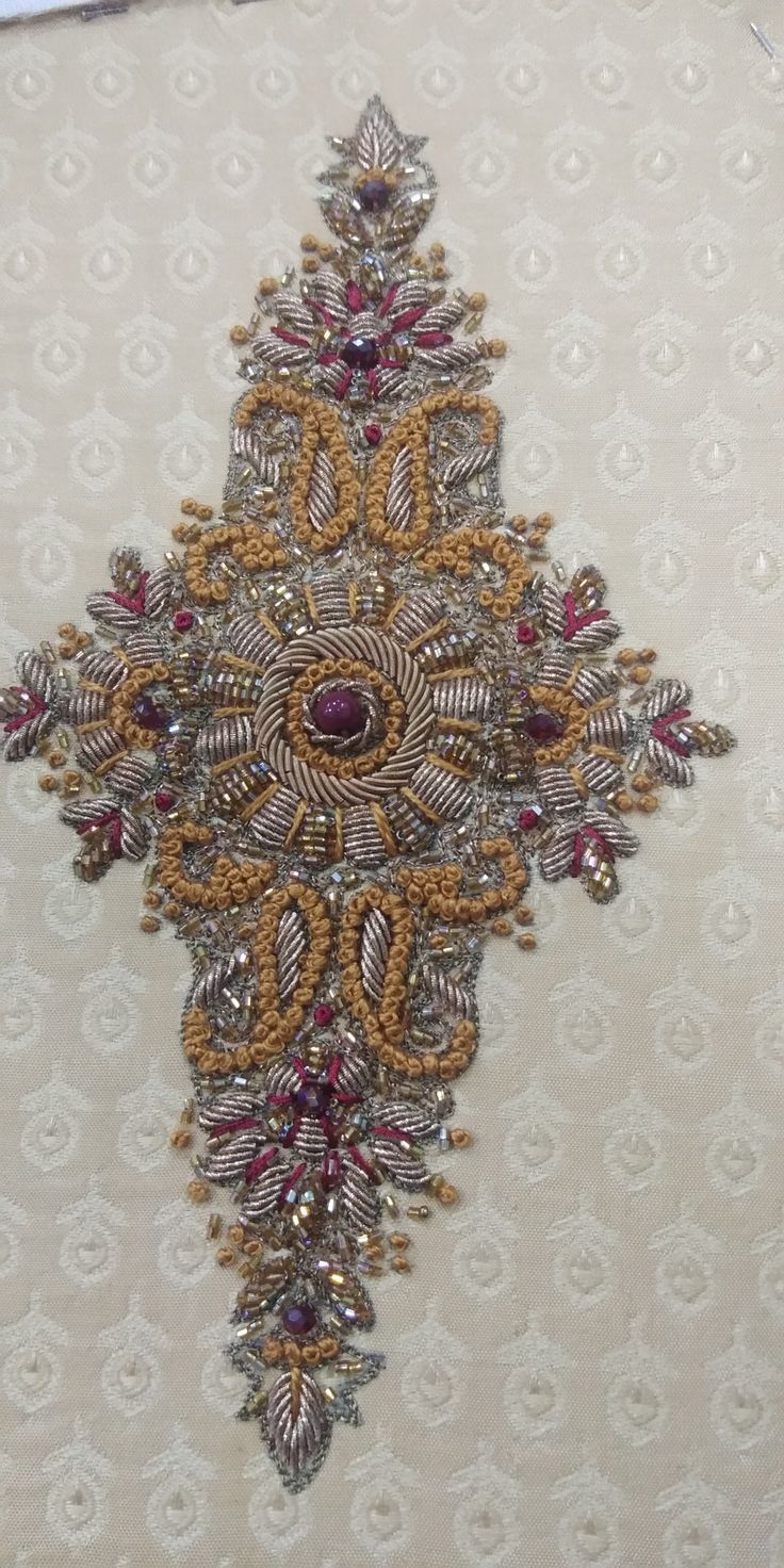 a cross made out of beads and stones on a white background with gold trimmings