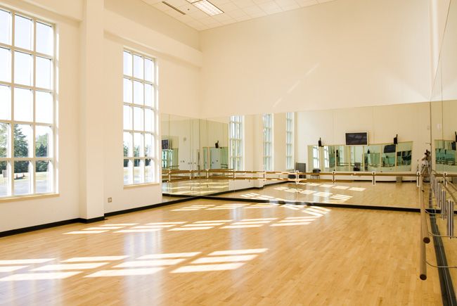 an empty dance studio with mirrors on the wall and hard wood flooring in front of large windows