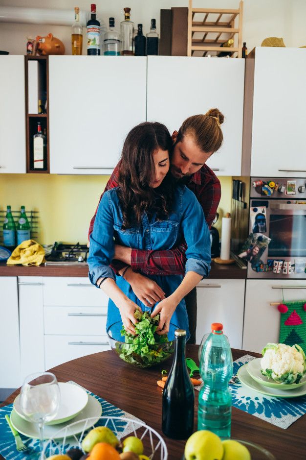 a man and woman standing in a kitchen preparing food on top of a wooden table