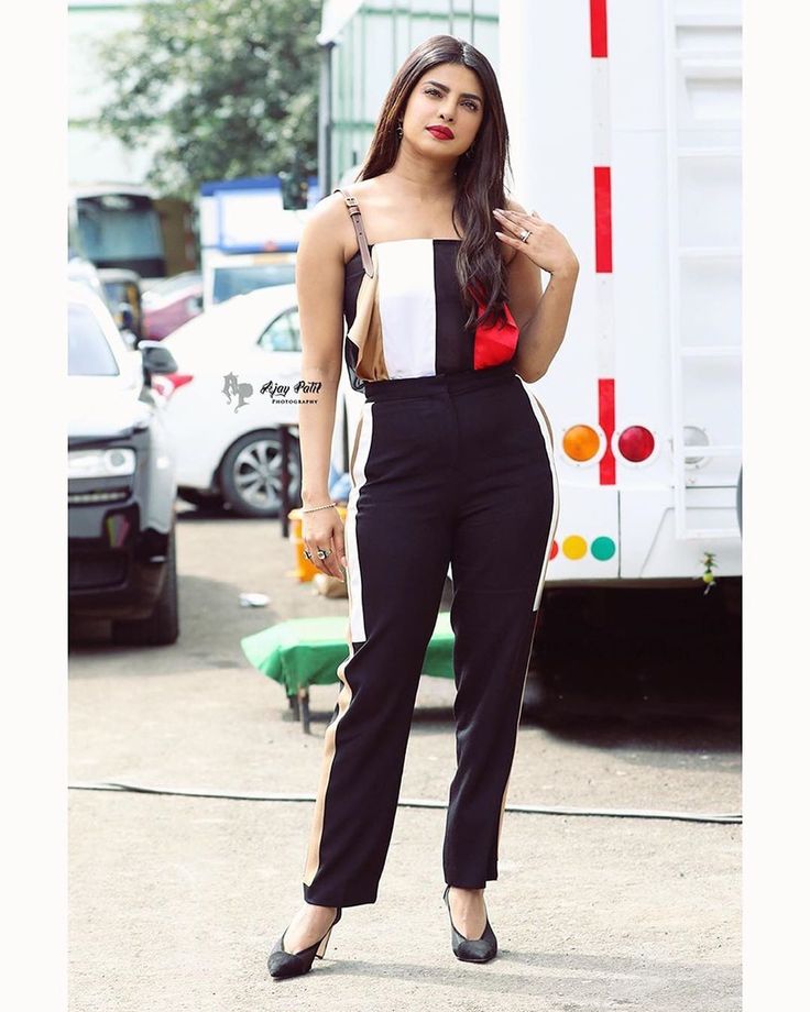 a woman standing in front of a white truck wearing black pants and a red bow tie