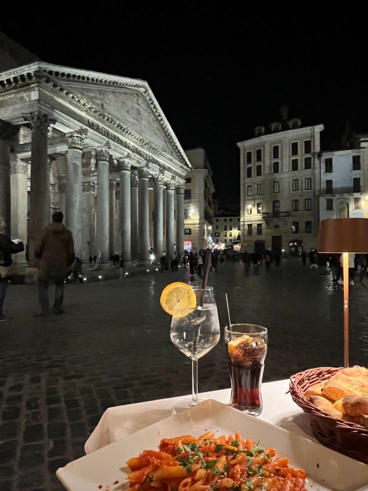 two plates of food are sitting on a table in front of an old building at night