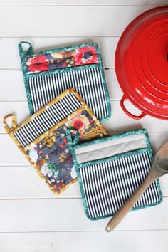 the pot holders are next to some utensils and a red pan on a white table