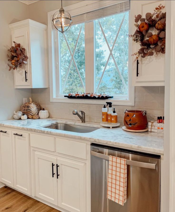 a kitchen with white cabinets and stainless steel dishwasher in the center, next to an open window