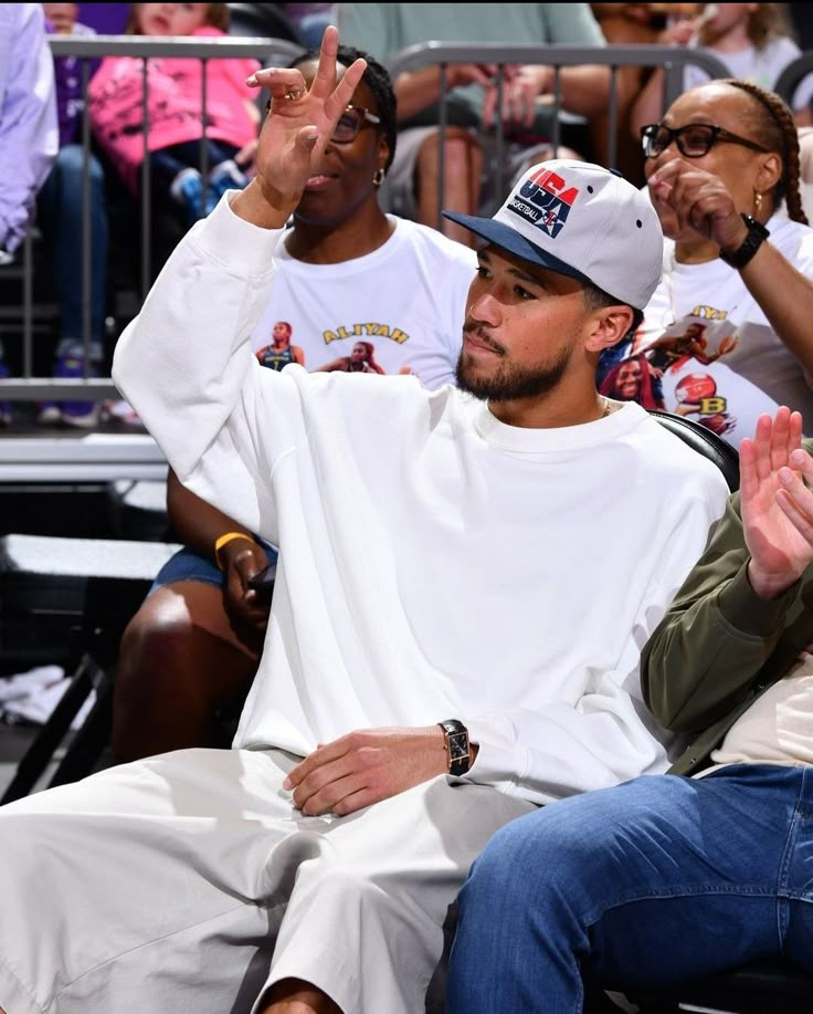 a man sitting in front of a crowd at a basketball game with his hand up