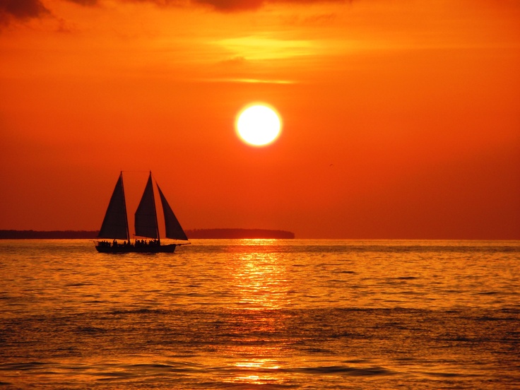 two sailboats are sailing in the ocean at sunset with an orange and red sky