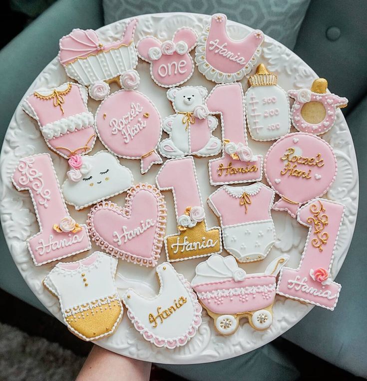 a white plate topped with lots of pink and gold decorated baby shower cookies on top of a table