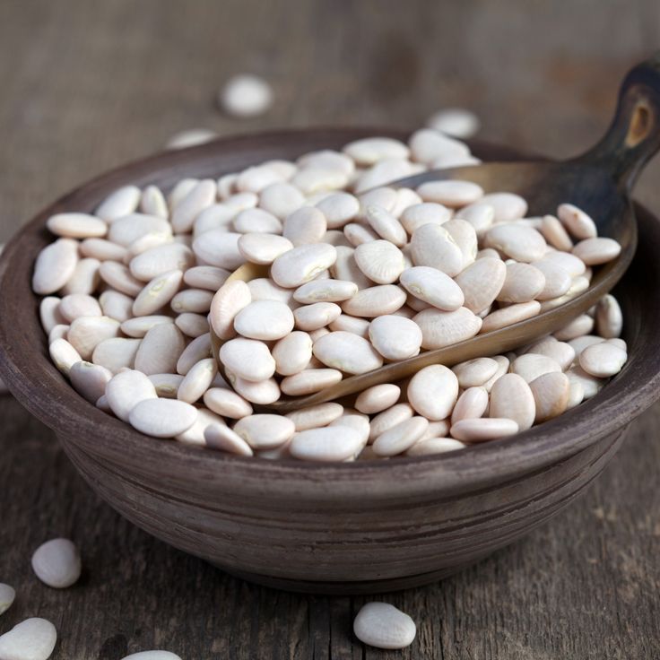 a wooden bowl filled with white beans and a spoon on top of it next to some seeds