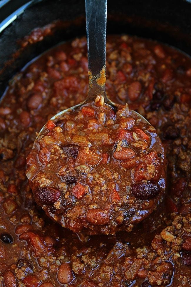 a ladle full of chili and beans in a crock pot with a spoon