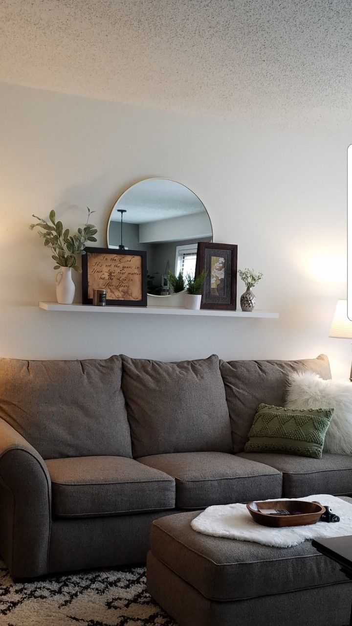 a living room with a couch, ottoman and mirror on the wall above it's headboard