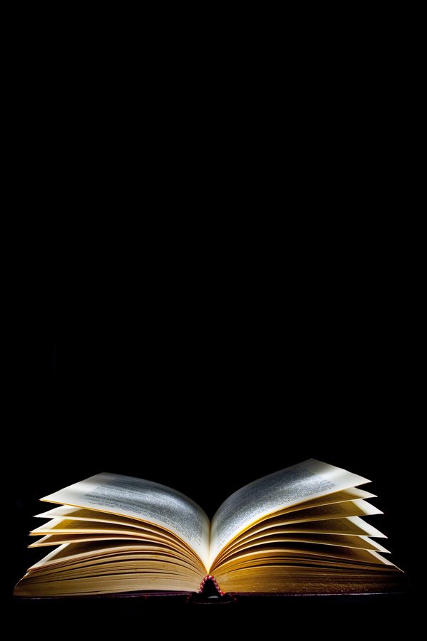 an open book sitting on top of a table in front of a black background with light coming from it