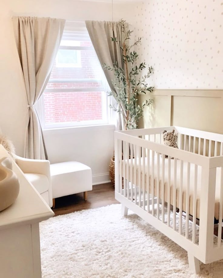 a baby's room with a white crib, chair and window in it