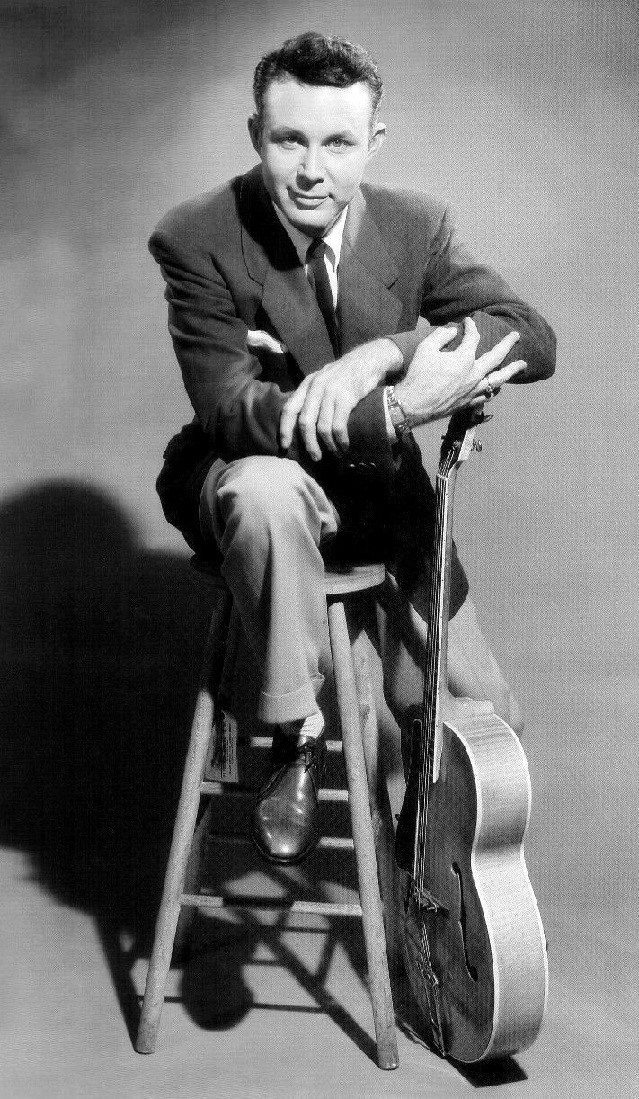 a man in a suit sitting on a stool with his legs crossed and holding a guitar