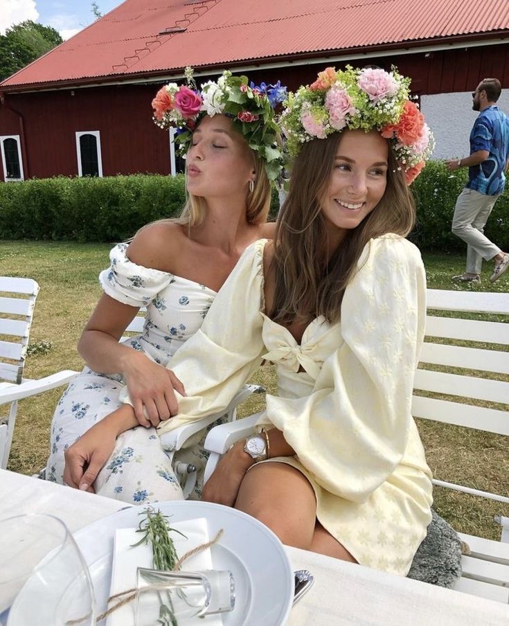 two young women sitting at a table with flowers in their hair and one wearing a flower crown