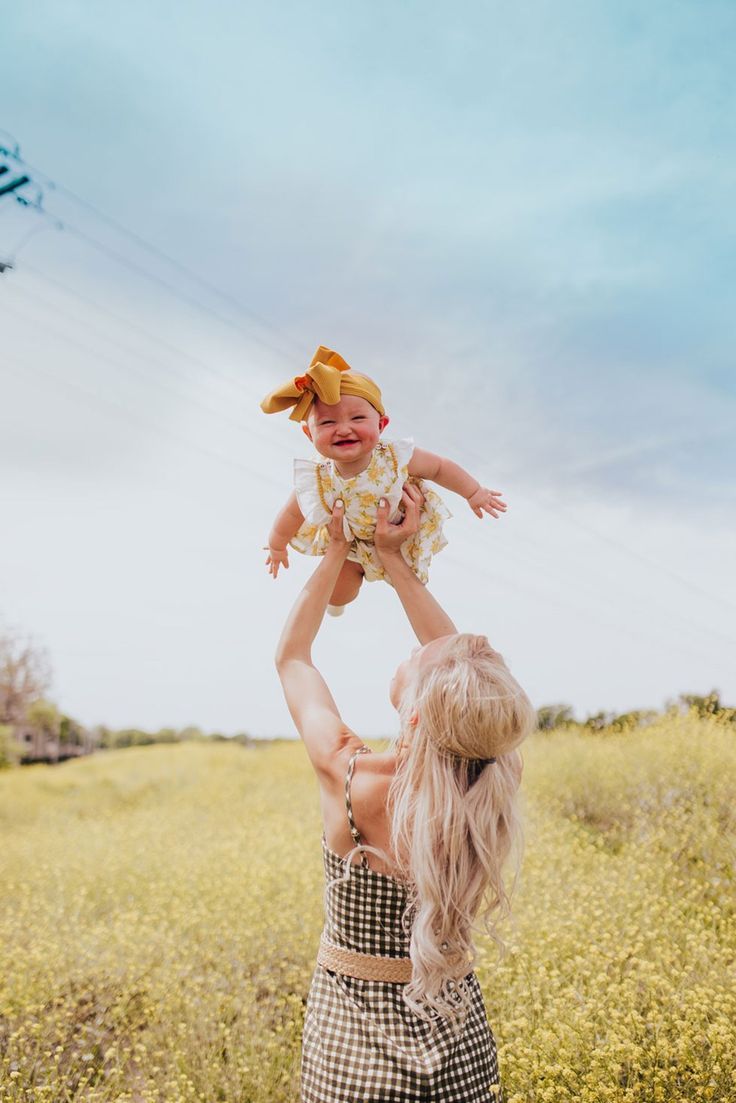 a woman holding a baby up in the air while standing on top of a grass covered field