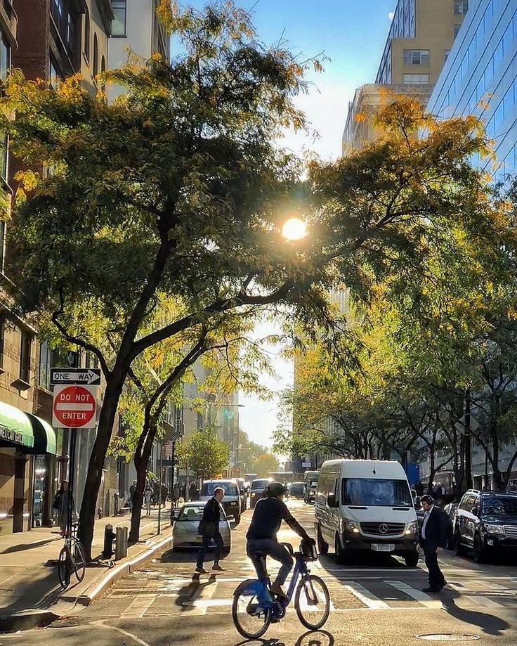 a man riding a bike down a street next to tall buildings and parked cars on the side of the road