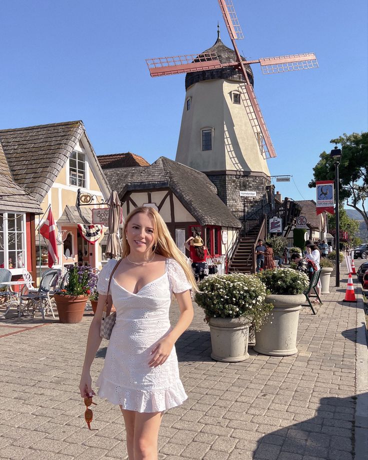 a woman standing in front of a windmill on a brick sidewalk with potted plants