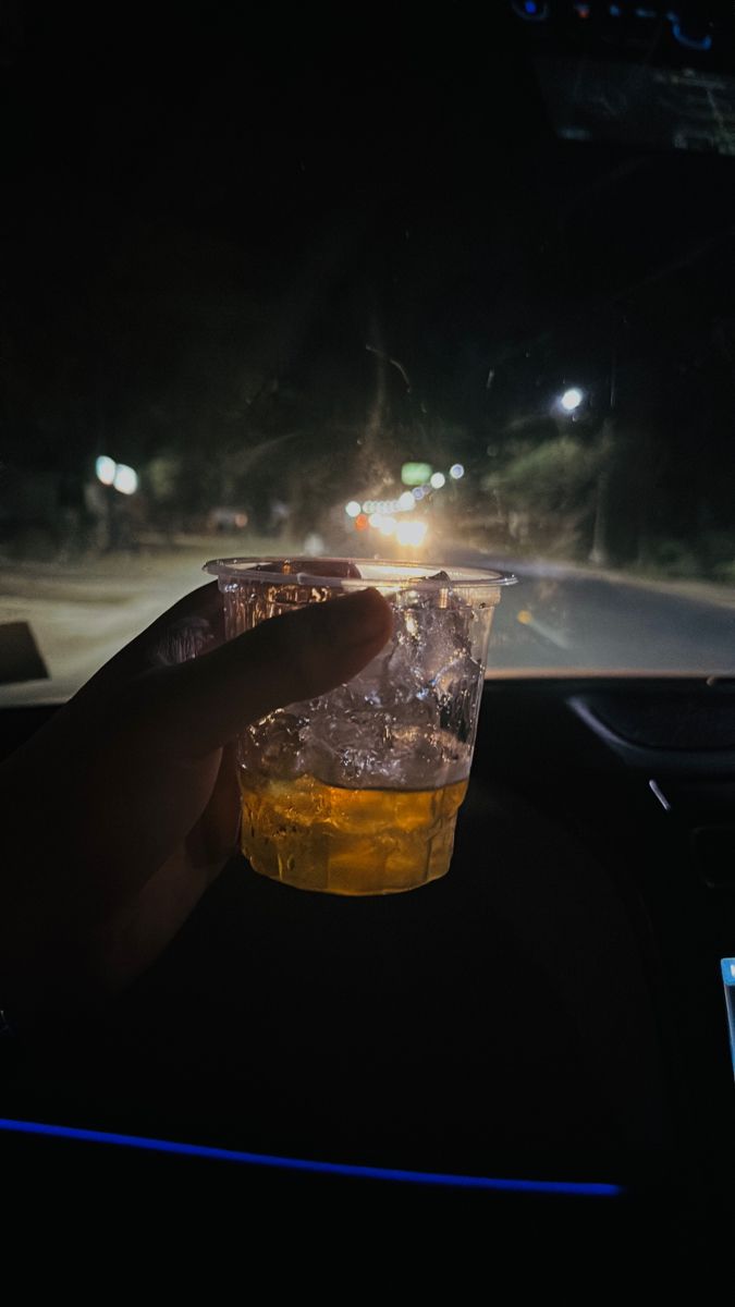 a person holding a cup in their hand while driving through the dark street at night