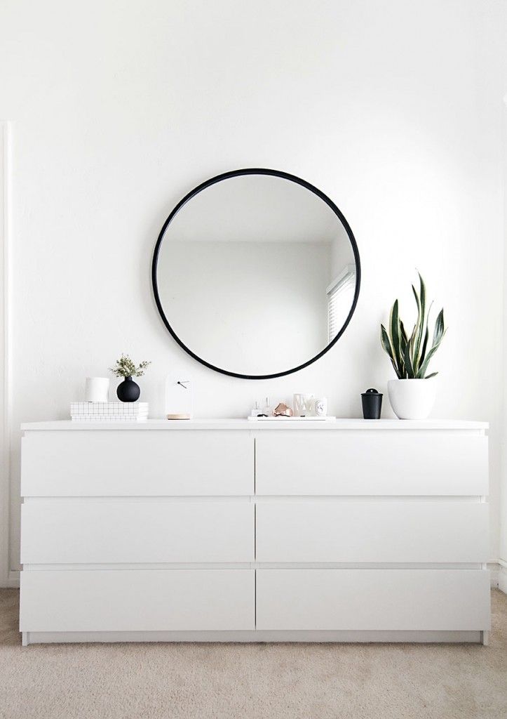 a white dresser with a round mirror above it and plants on the top shelf in front of it