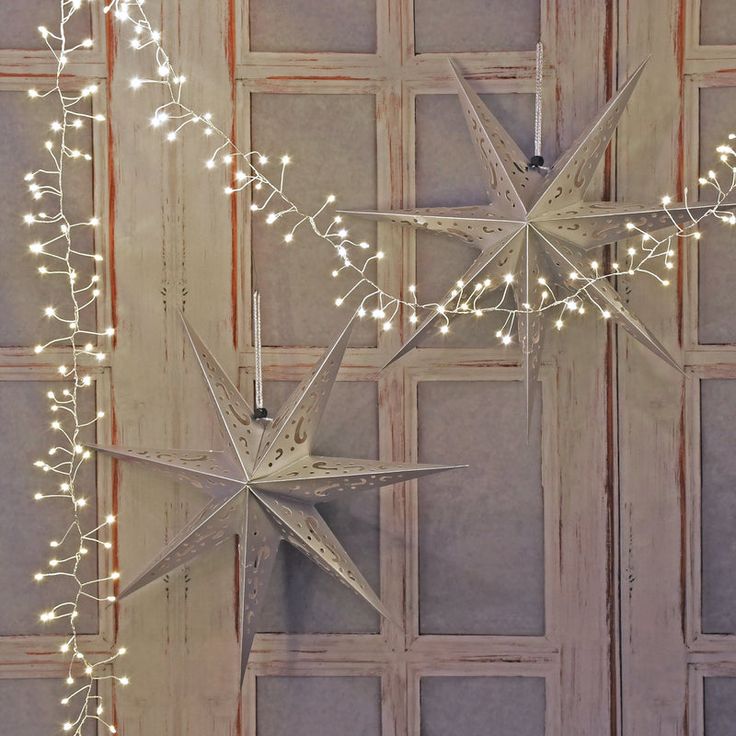 three white stars with lights hanging from them in front of a wooden paneled wall