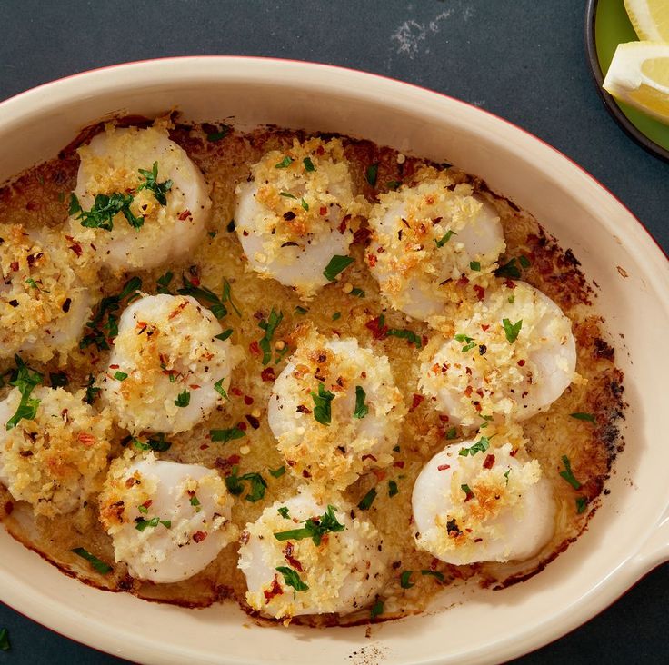 a white dish filled with scallops and garnished with parmesan cheese