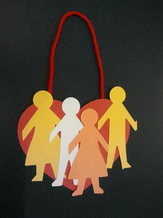 an ornament with paper cutouts of people holding hands and heart on black background