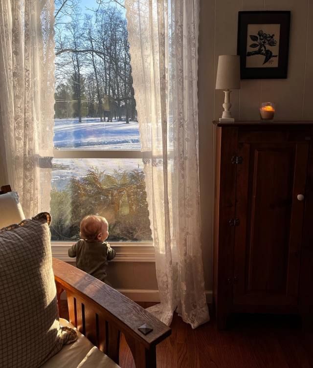 a small child sitting in front of a window looking out at the snow covered ground