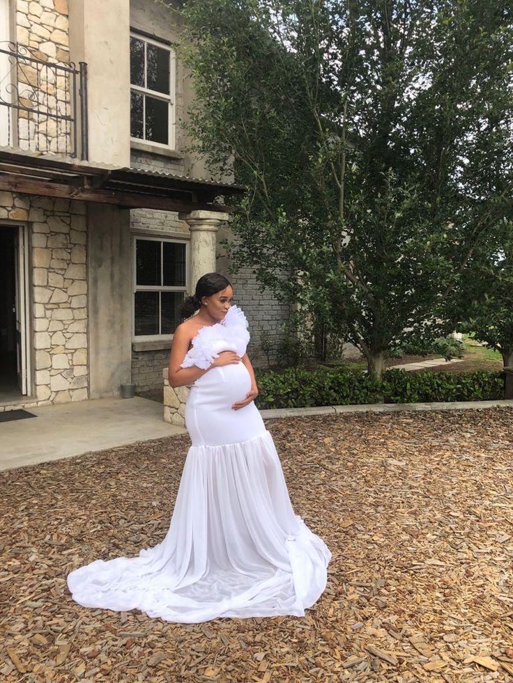 a pregnant woman standing in front of a house wearing a white dress and holding her belly