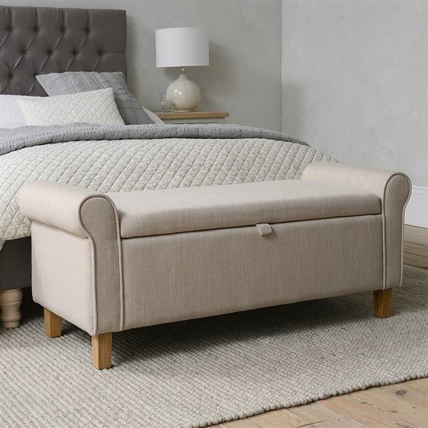 a bed with a gray headboard and footstool sitting on top of a rug