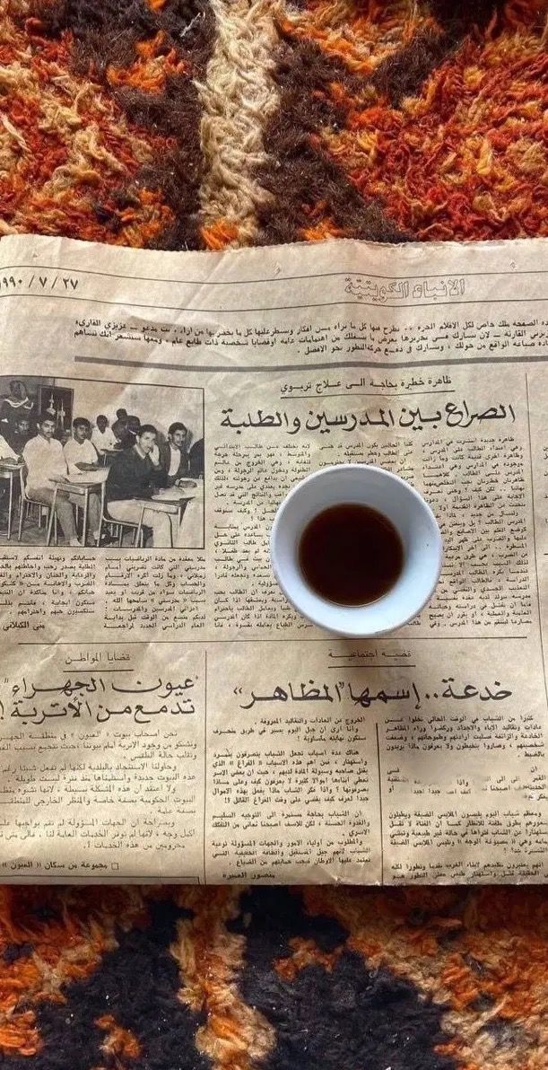 a cup of coffee sitting on top of a newspaper with some writing in arabic and english