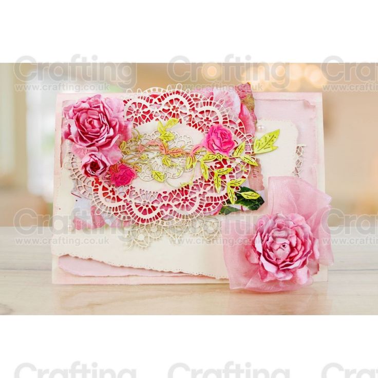 a close up of a card on a table with pink flowers and paper doily