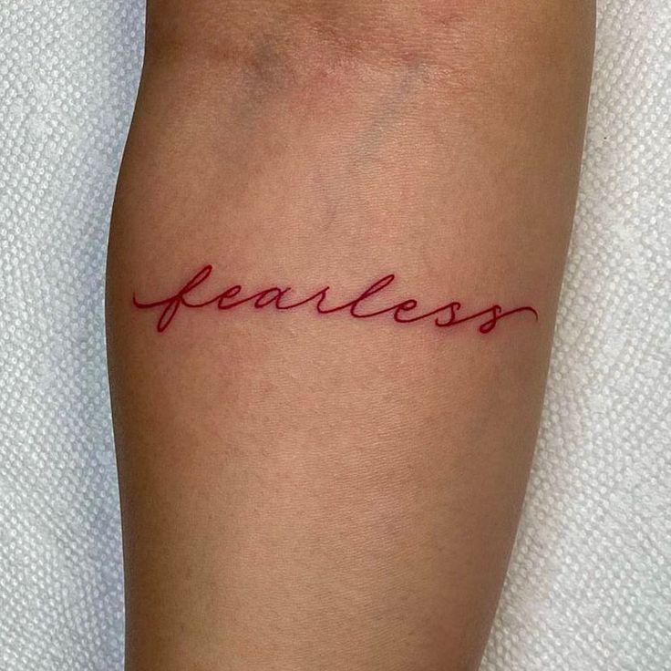 a woman's arm with the word fearless tattooed on her left calf and red ink that reads fearless