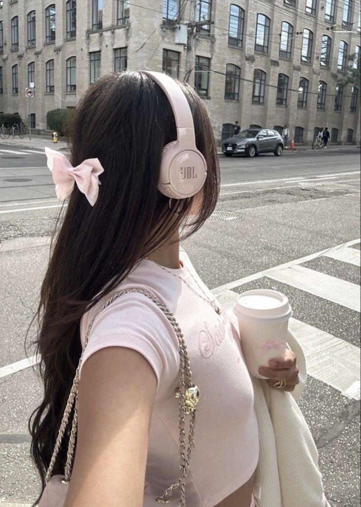 a woman with headphones on walking down the street while holding a coffee cup in her hand