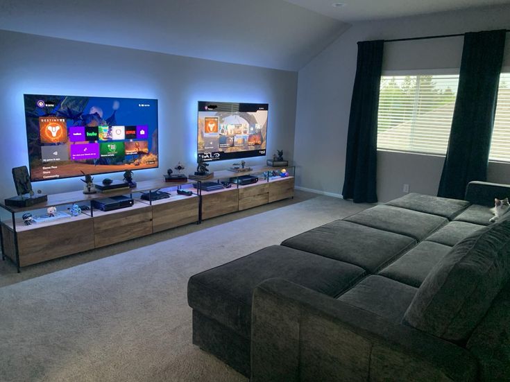 a living room filled with furniture and two flat screen tvs mounted on the wall