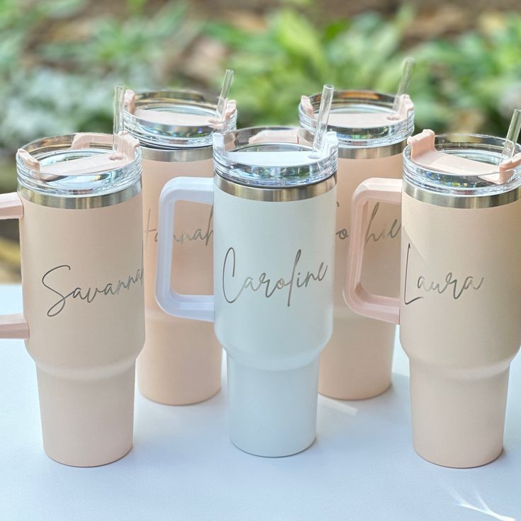 four coffee mugs with names on them are sitting next to each other in front of some bushes