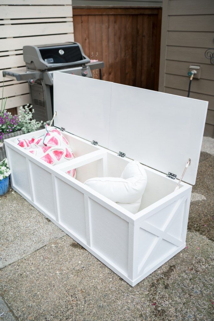 an open storage box sitting on the side of a building next to flowers and a grill