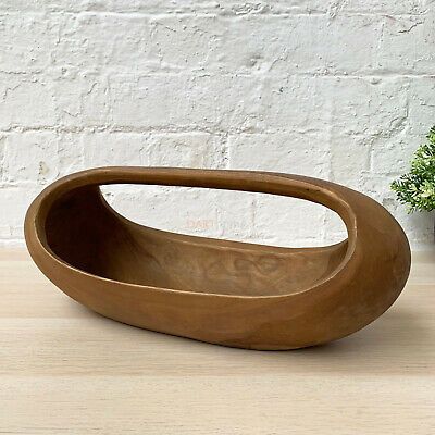 a wooden bowl sitting on top of a table next to a potted plant in front of a white brick wall