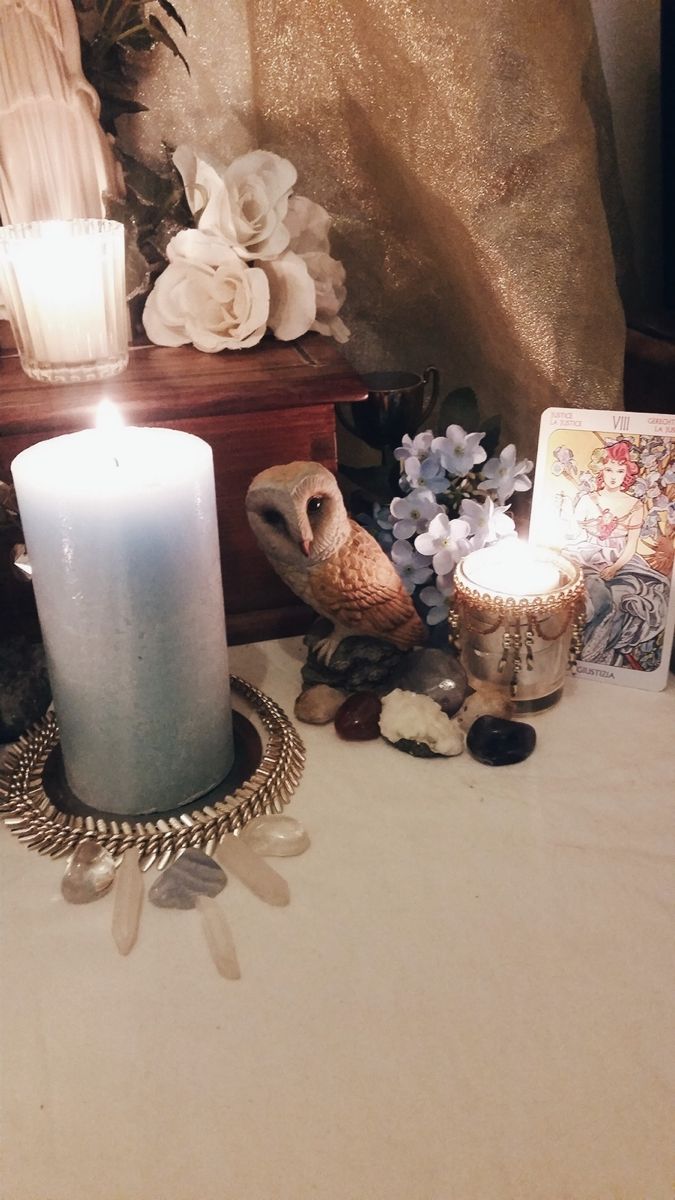 an owl sitting on top of a table next to a lit candle and pictures with flowers