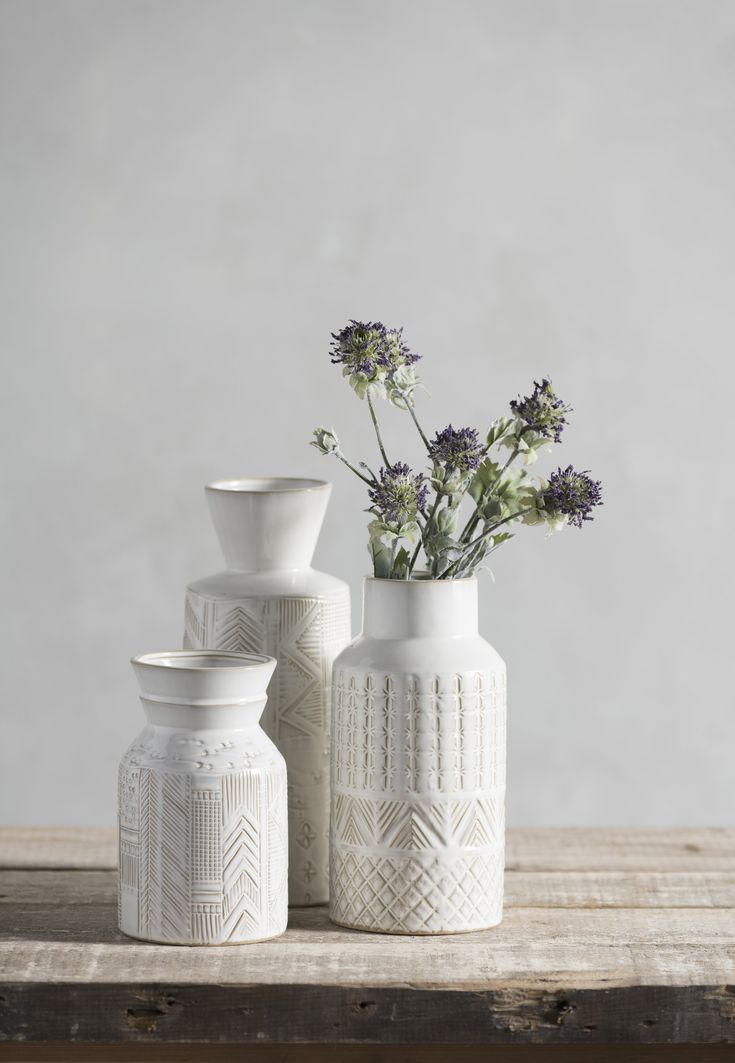 three white vases sitting on top of a wooden table