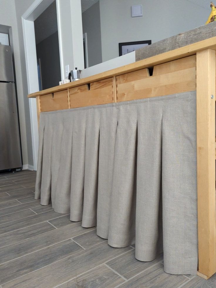 a kitchen counter that has some curtains on it and a refrigerator in the back ground