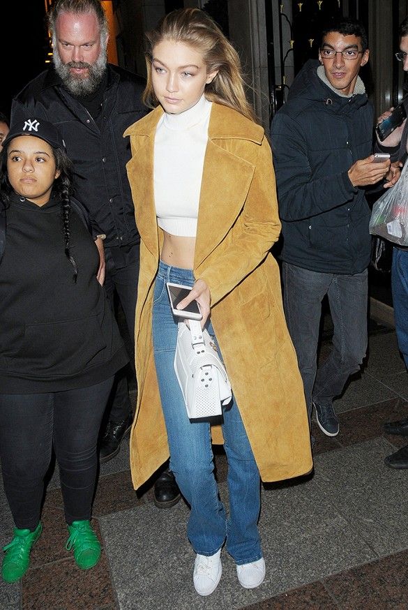 a woman in jeans and a coat is walking down the street with her hand on her hip