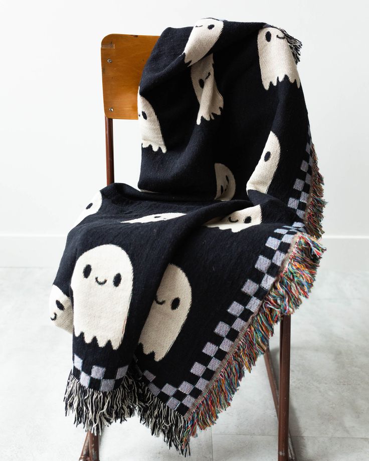 a black and white blanket with ghost faces on it, sitting on a wooden chair