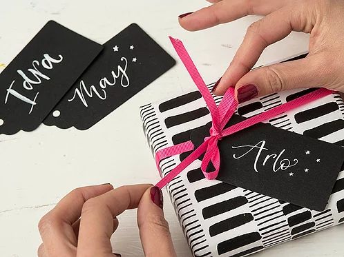 two hands holding a gift wrapped in black and white wrapping paper with pink ribbon on it